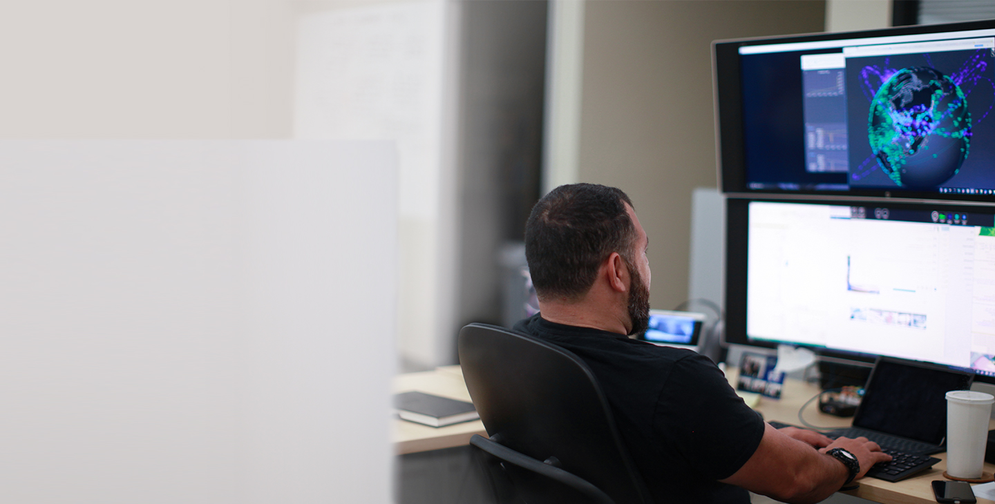 Man sitting at a desk looking at two monitors stacked on top of each other and typing on a keyboard