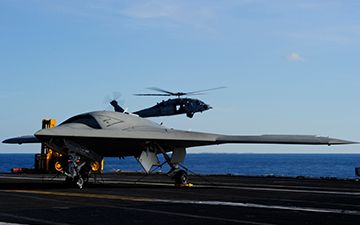 Fighter jet on the runway of a ship at sea and a helicopter flying in the background