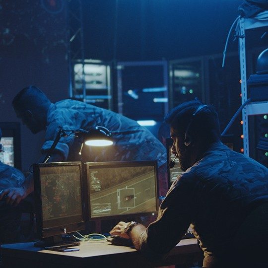 3 men in a room using a tactical communications to monitor a mission