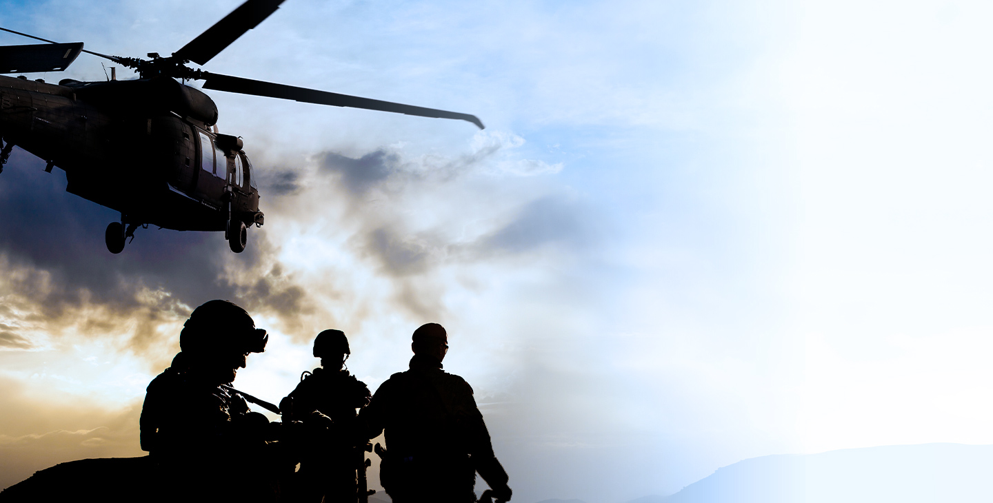 Silhouettes of three soldiers at dusk with a helicopter flying overhead