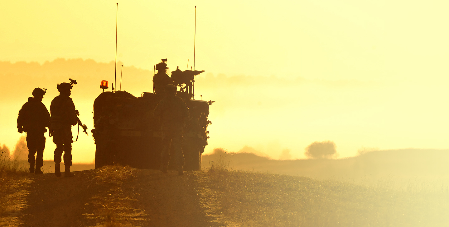 Four soldiers at dusk with a military vehicle utilizing mobile integrated solutions for tactical operations