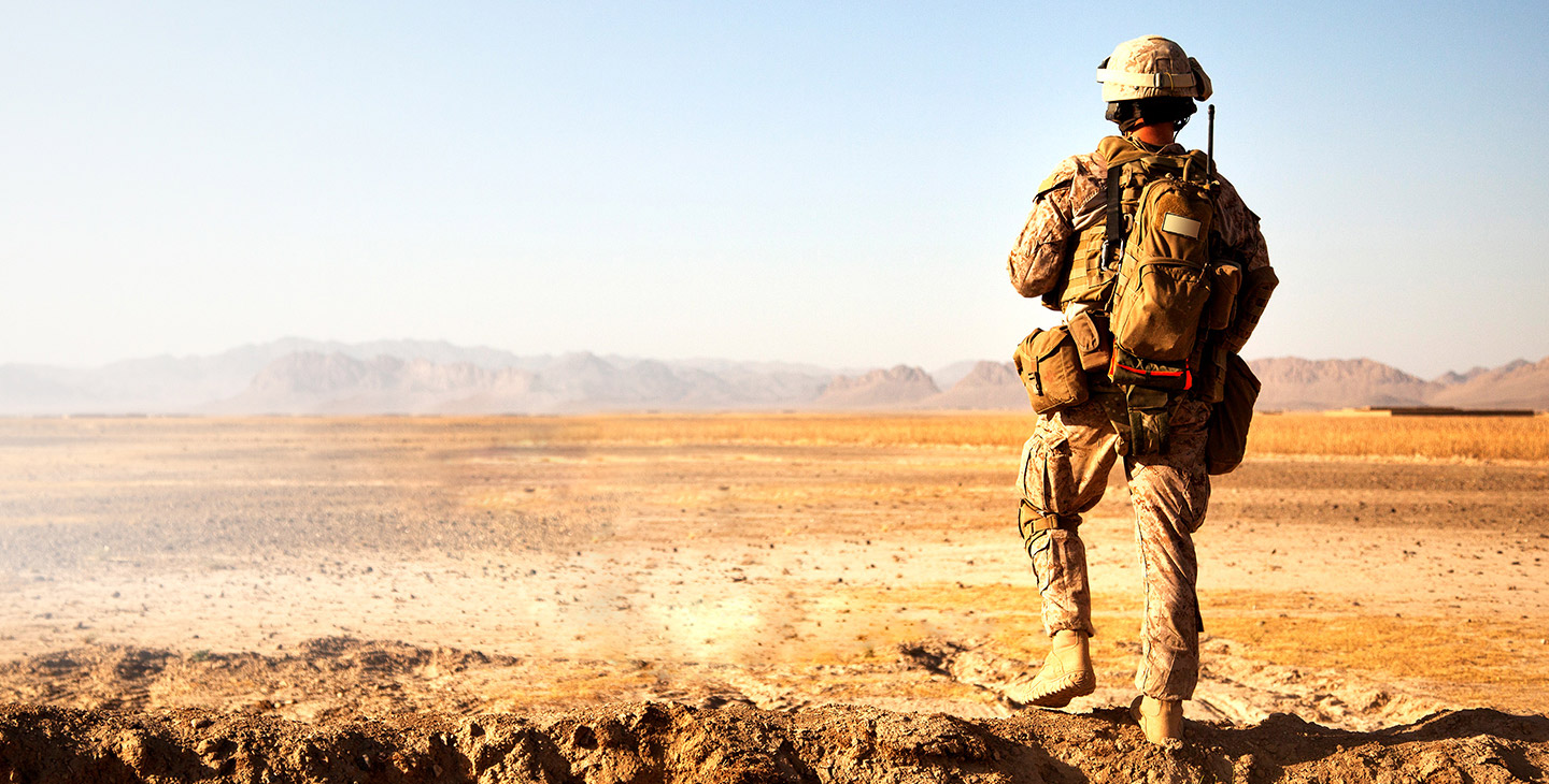 Back of a soldier in the desert, derssed in army gear and backpack