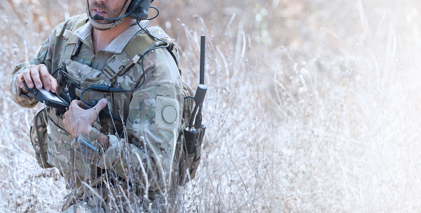 Solider in green camo standing in tall shubbery with his hand on an ELITE wearable kit