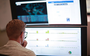 Back view of a man wearing glasses looking at two large, stacked monitors