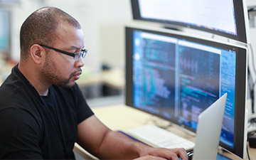 Man sitting at a desk with stacked monitors, working on a laptop