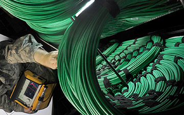 Aerial view of a man dressed in camo reaching up towards coils of green cables