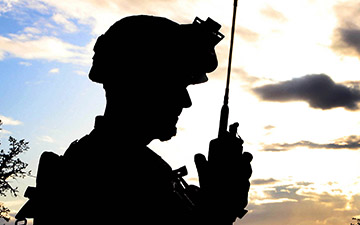 Silhouette of a soldier talking on a handheld radio at disk