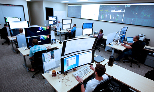 Viasat employees working at desks with 2 large, stacked monitors at a cybersecurity operations center