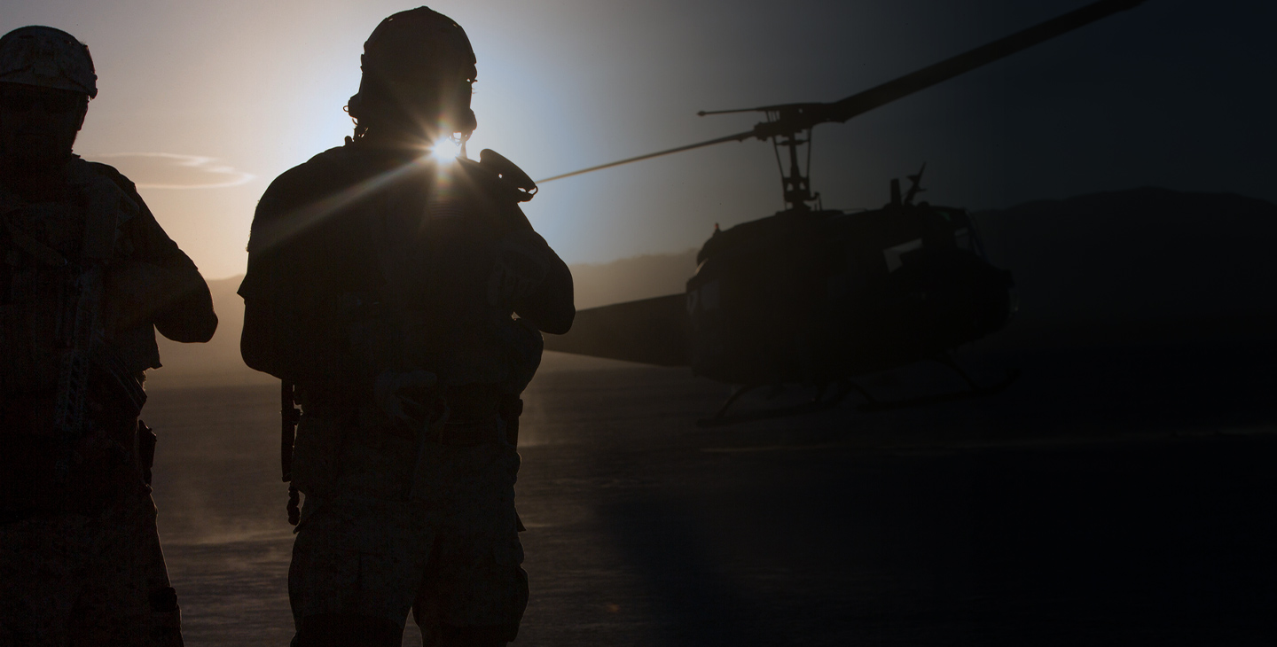 Two silhouettes of soldiers watching a helicopter take off