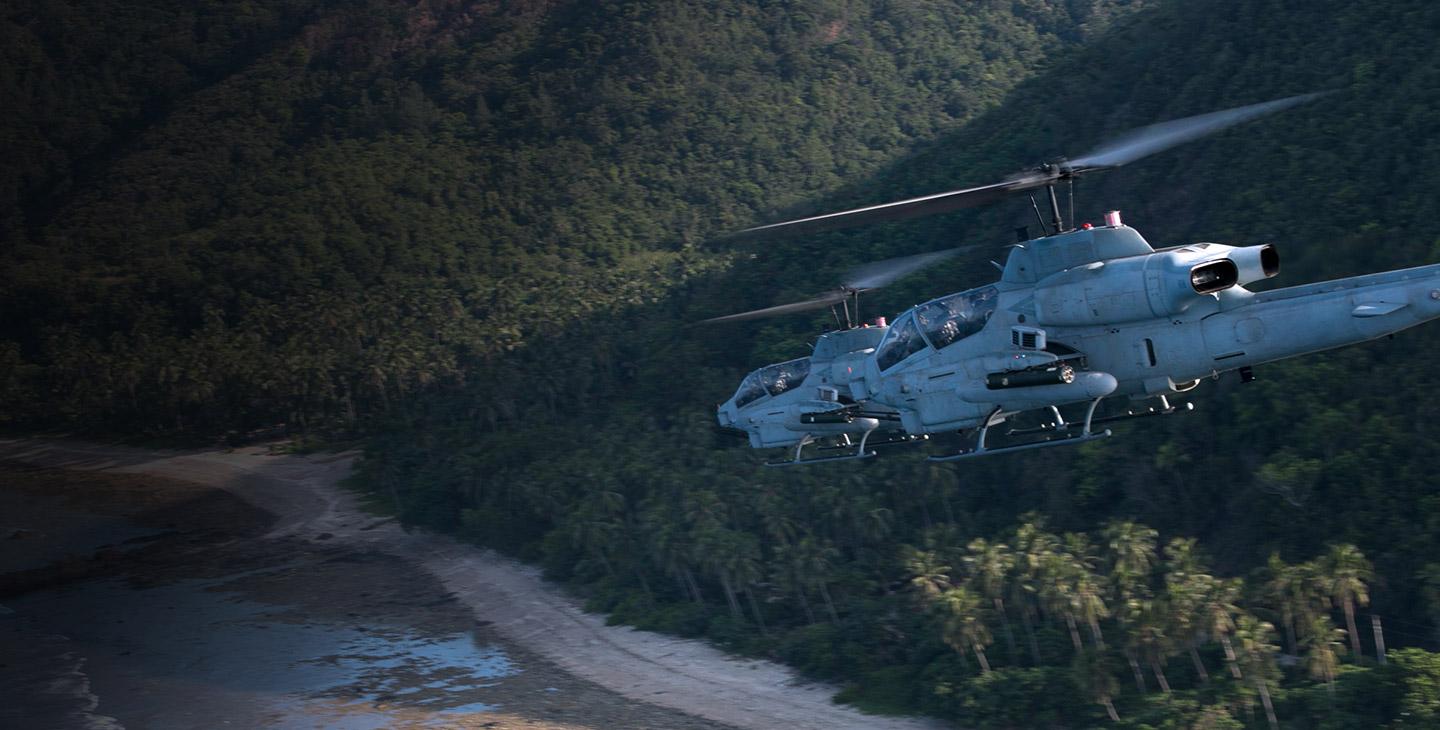 Two military helicopters flying over a coastline