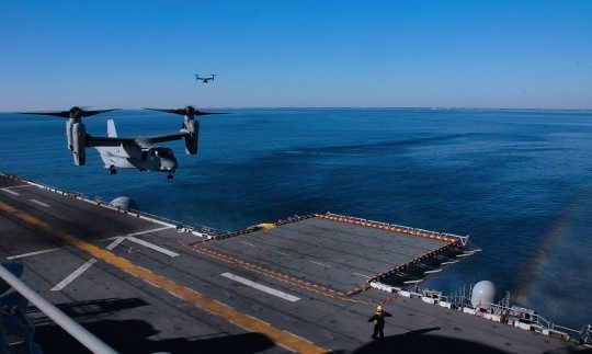 Two loarge military planes approaching a landing pad on a ship at sea