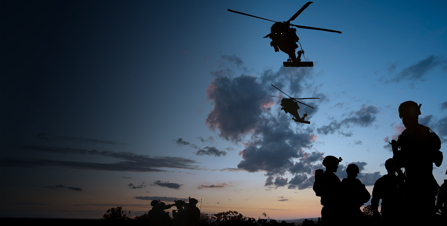 Rotary wing aircraft flying over soldiers utilizing defense technology at dusk