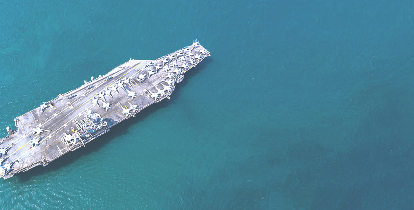 Aircraft carrier carrying many fighter jets across a blue-green ocean 