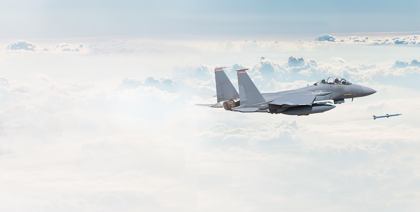 Gray fighter jet flying above the clouds with a missle airborne below
