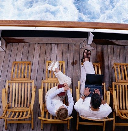 Overhead view of a man and woman sitting on a boat deck at sea, using marine internet on a laptop.