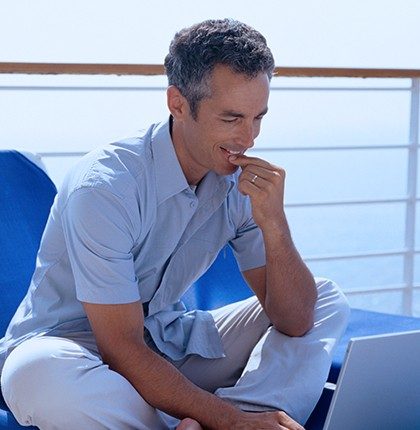 Man sitting on the deck of a passenger boat using a laptop with satellite internet for boats