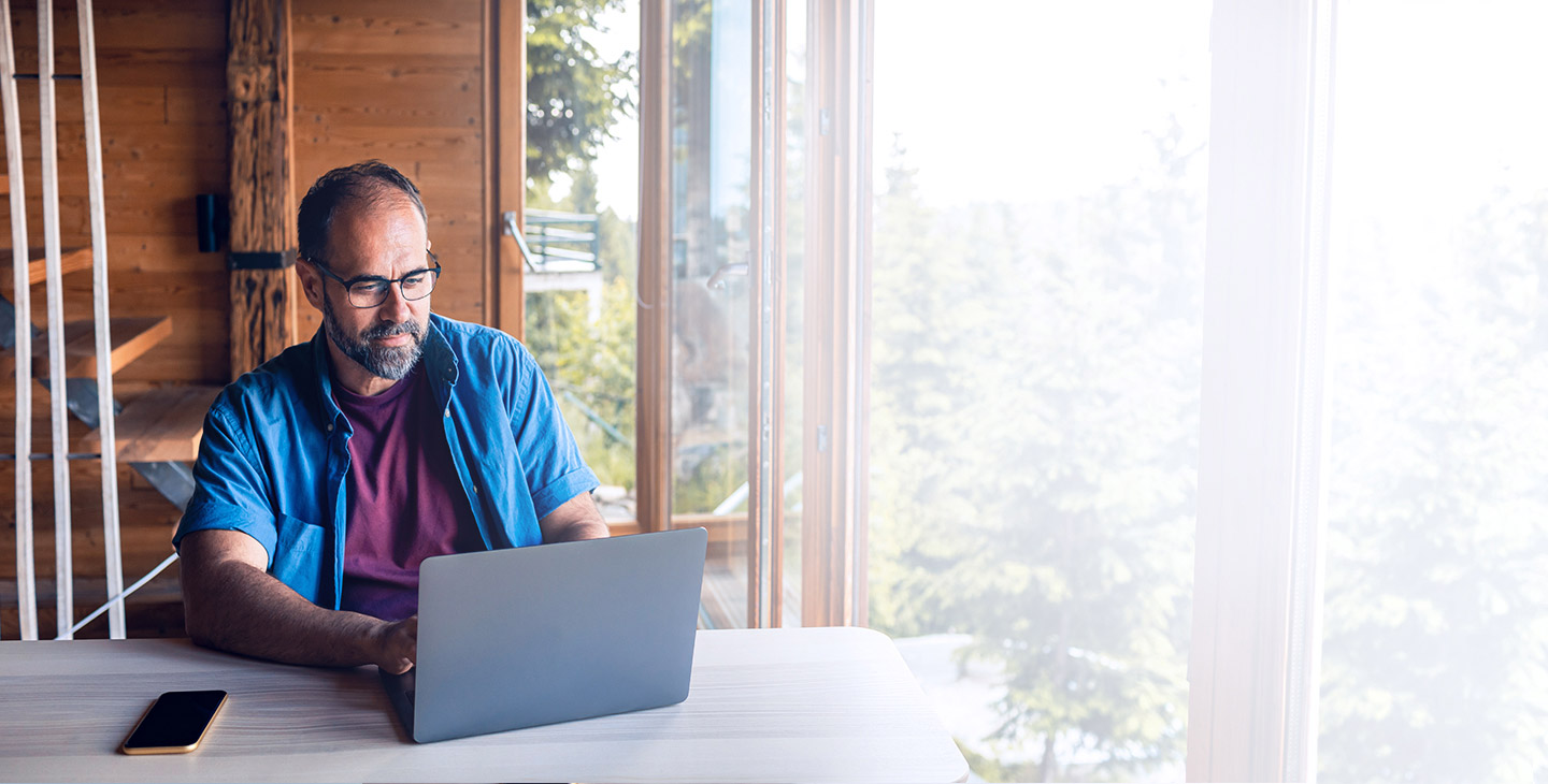 Man with a home wifi plan sitting at a table in his mountain house on a laptop 