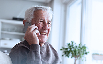 Older man talking on a cell phone in his home utilizing VoIP, a Viasat internet add-on