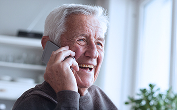 Older man talking on a cell phone in his home utilizing VoIP, a Viasat internet add-on