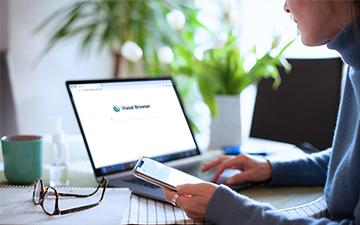 Woman holding her cell phone, sitting at a laptop featuring the Viasat Browser