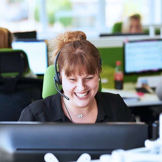 A woman working in a sales call center is smiling, talking to a customer about Viasat EasyCare