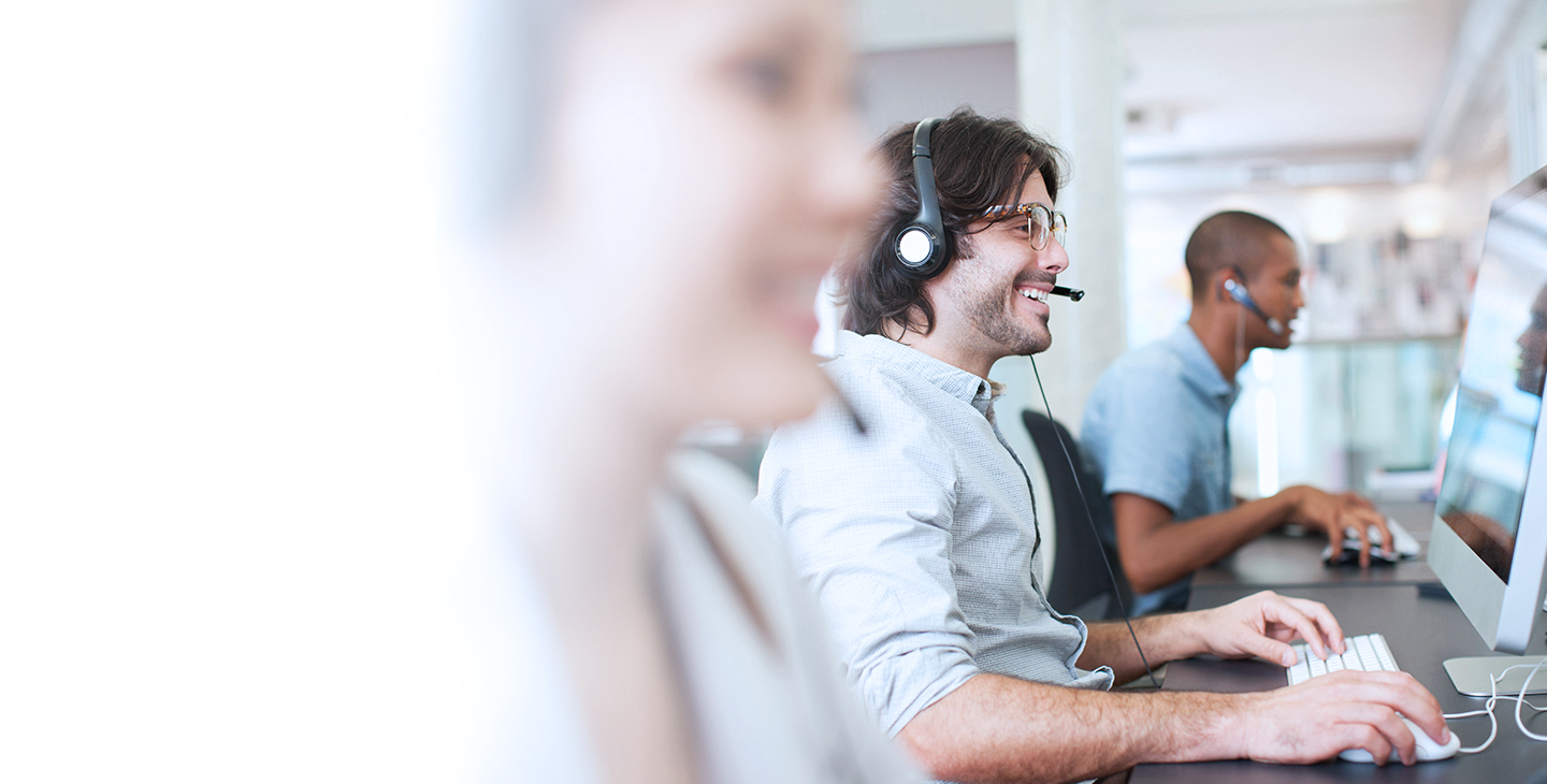 A row of people working at their computers at a call center wearing headsets