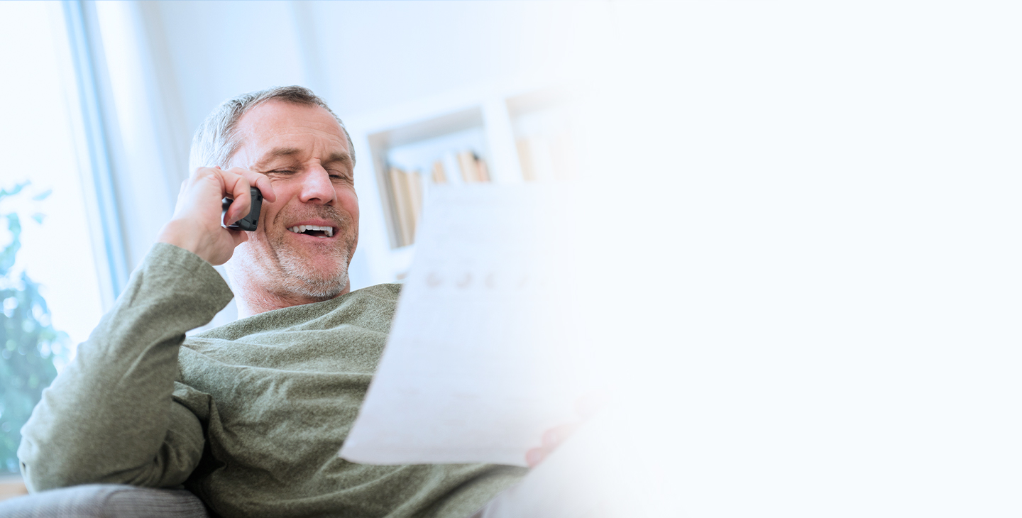 A man sitting on a couch looking at a piece of paper, talking on his VoIP home phone