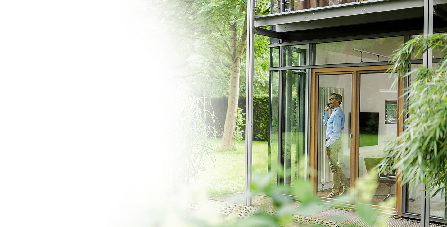 A man standing and looking out large windows in his house talking on his VoIP home phone