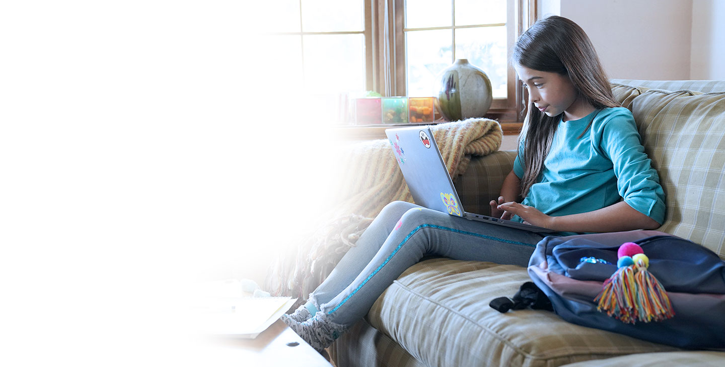 Young schoolgirl feels safe with Viasat's internet security software, doing homework on a laptop on the couch