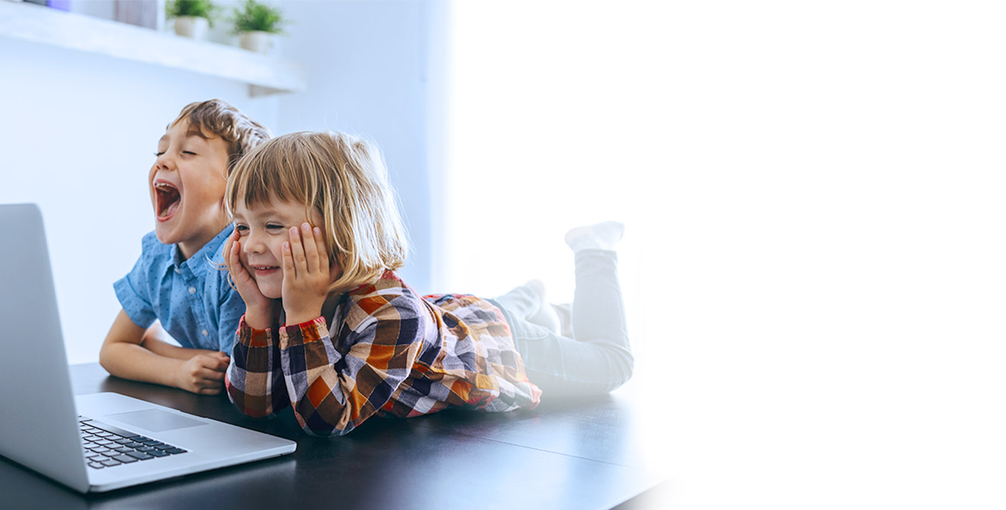 A little girl and little boy are protected with internet security software and are laying on the floor laughing at a laptop