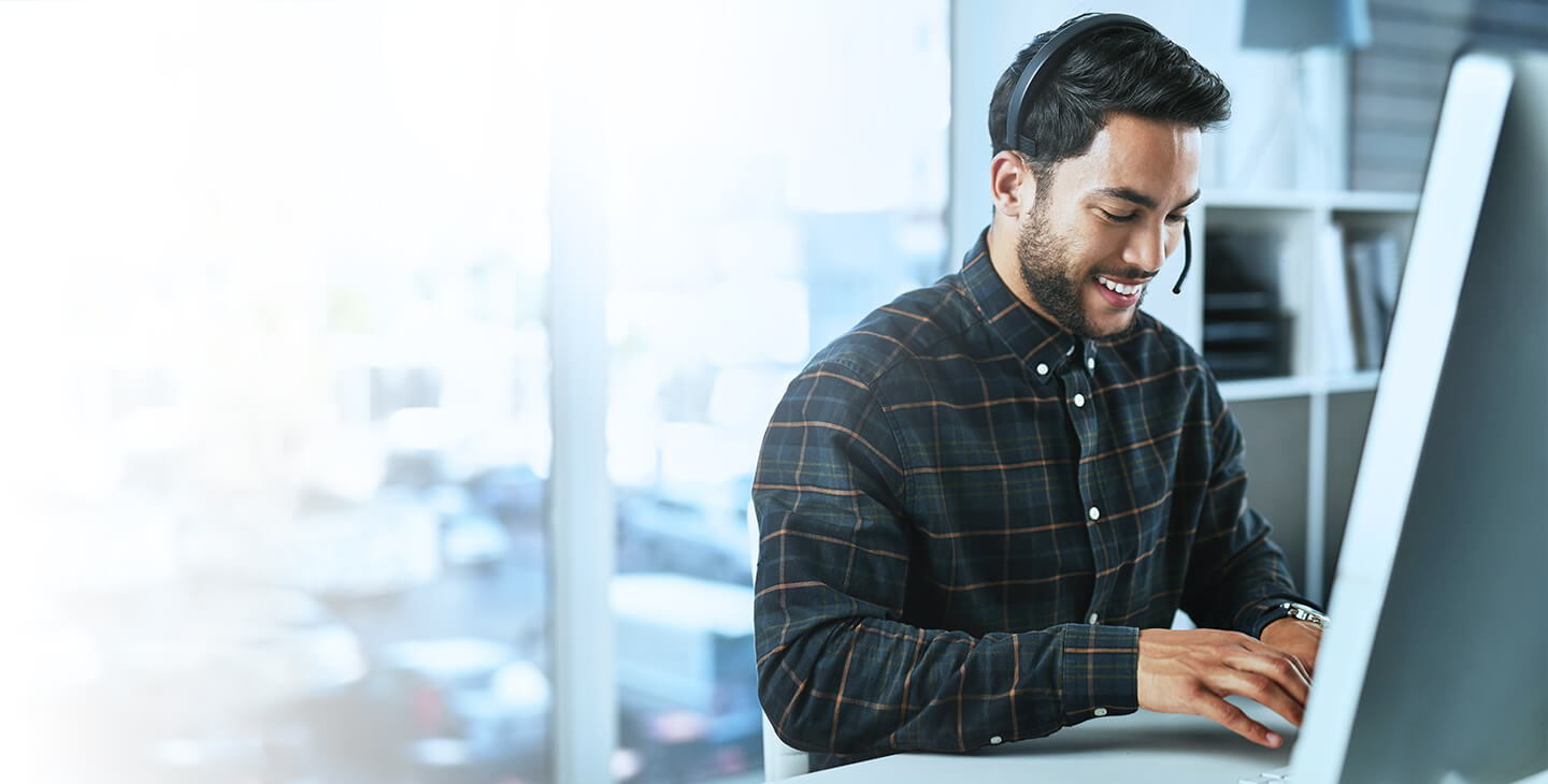 A man wearing a plaid shirt and a headset, searching for a Viasat satellite dealer near him on his computer