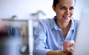 Woman sitting in front of her computer, drinking coffee and smiling