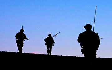 Silhouette of three soliders in the field at dusk against a fading blue sky