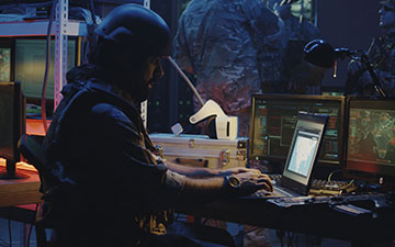 Man wearing combat gear sitting at a small laptop, utilizing Viasat services in the field