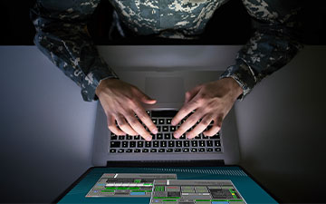 Aerial view of a man wearing a camo uniform sitting at a laptop utilizing Viasat software