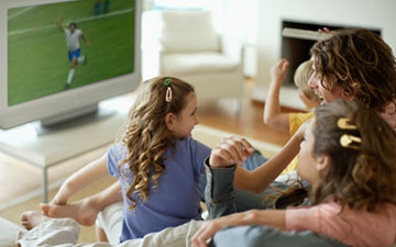 Family of four sitting on the couch watching soccer on TV