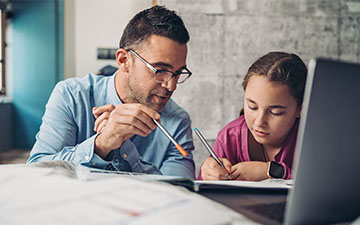 Man using Viasat services to help his daughter with homework at a table covered in books and a laptop