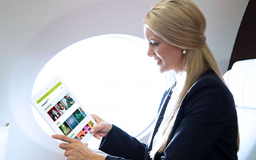 Blonde business woman sitting on a private jet looking at content on a tablet