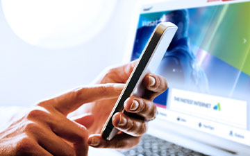Close-up of a hand interacting with a smartphone in front of a laptop while seated on a plane
