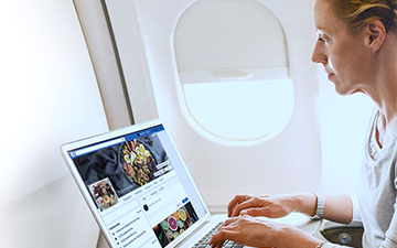 Blonde woman sitting on a plate with a latptop on a tray table, surfing Facebook