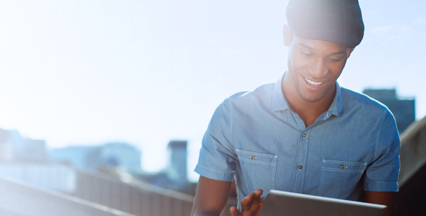 Man smiling, wearing a flat cap and blue button-down shirt, holding a tablet using Viasat services