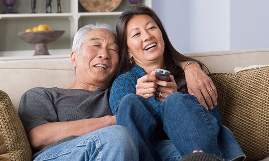 A man has his arm around a woman holding a DISH satellite TV remote on the couch