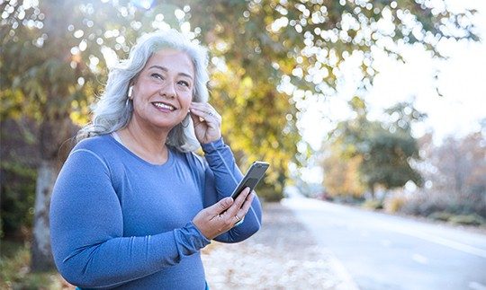 A woman standing outside with Apple earbuds talking on home VoIP service in front of a tree