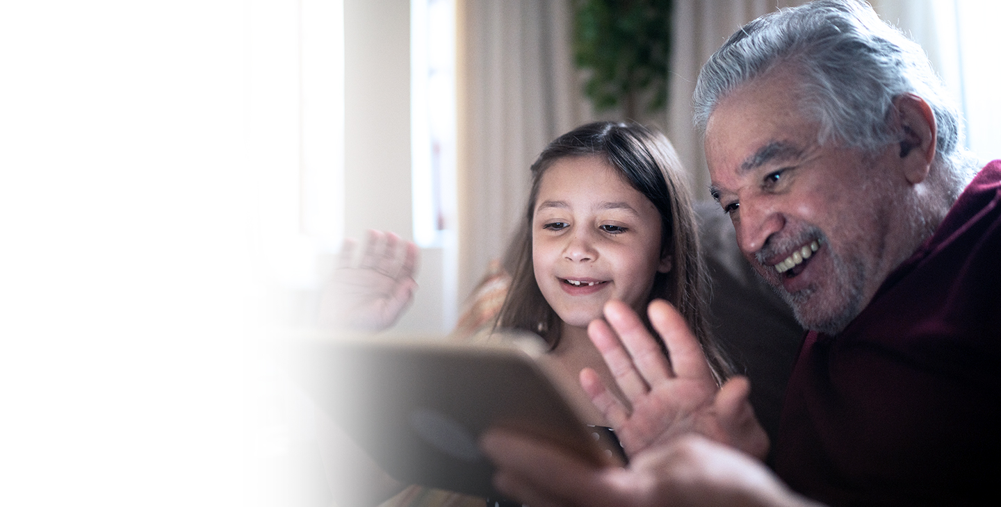Child sitting with her grandfather waving and staying connected through a video conference on their tablet