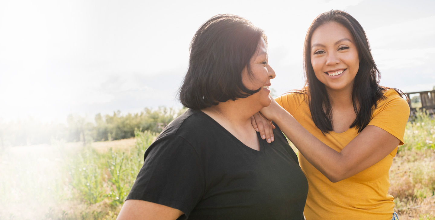 Two women smiling and standing shoulder to shoulder in an open field, excited to have affordable satellite internet with help from Viasat and the FCC's Affordable Connectivity Program.