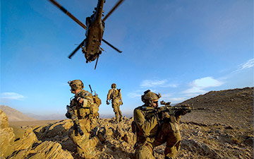 Three soldiers on watch out in the field with a helicopter flying above